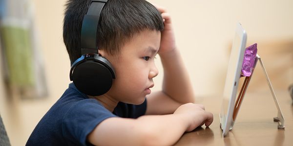 Barn sidder med høretelefoner på og interagerer med en tablet