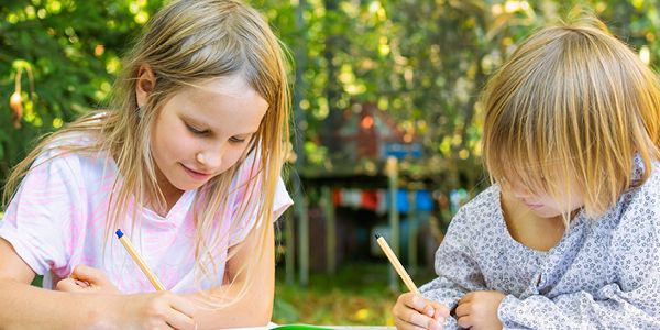 To børn sidder i naturen og tegner
