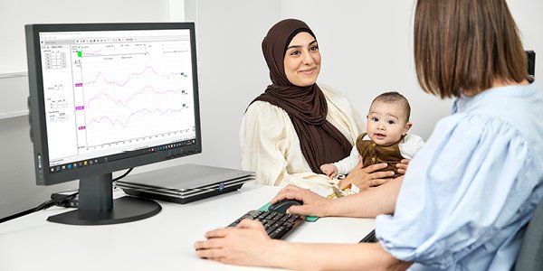 En baby sidder hos sin mor, mens en audiolog taler med moderen om Aided Cortical-testen