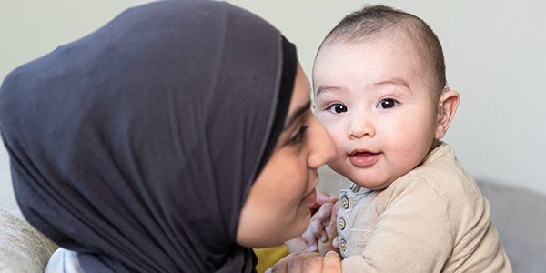 En baby sidder hos sin mor og smiler til kameraet